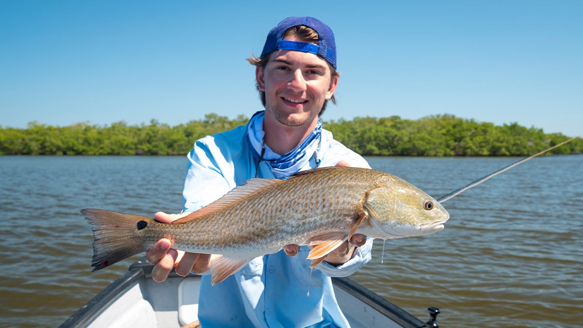 An angler holds up a redfish caught on the fly.