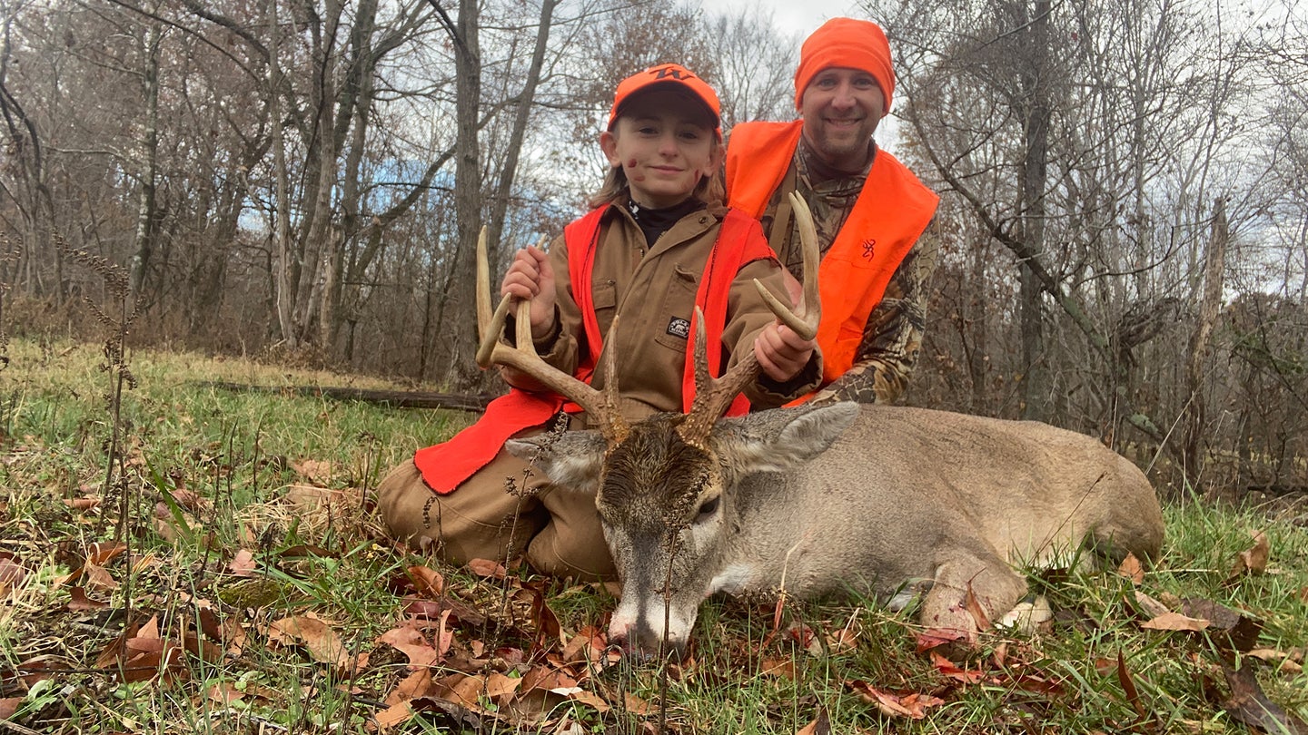 A young hunter and his dad, both wearing blaze orange, pose with a nice whitetail buck.