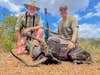 Two hunters kneel behind an African black impala ram.