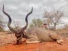 A hunter sits on the red-clay ground behind a big African kudu. 