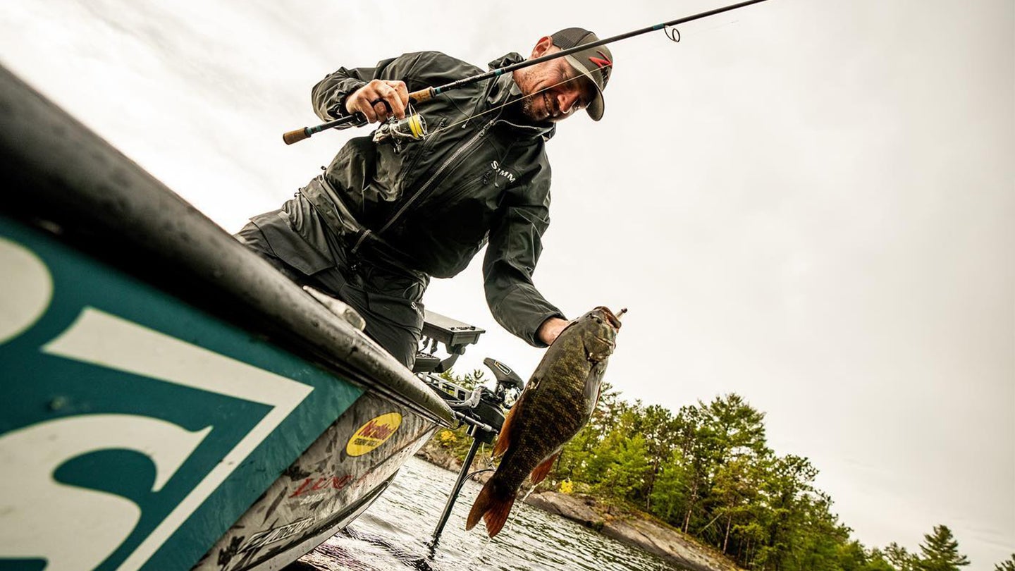 An angler in a boat lands a big smallmouth bass with a spinning rod.