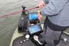 And angler on a lake in a bass boat with a panel of electronic fishfinders at his feet.