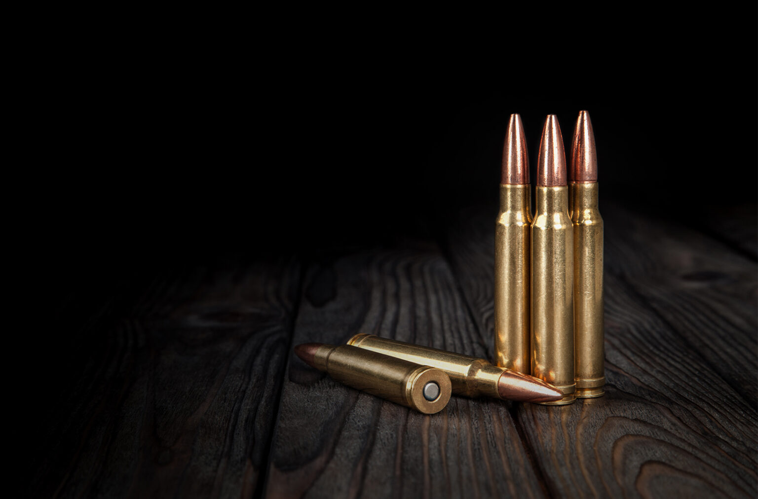 Rifle cartridges on a wood surface with dark background.