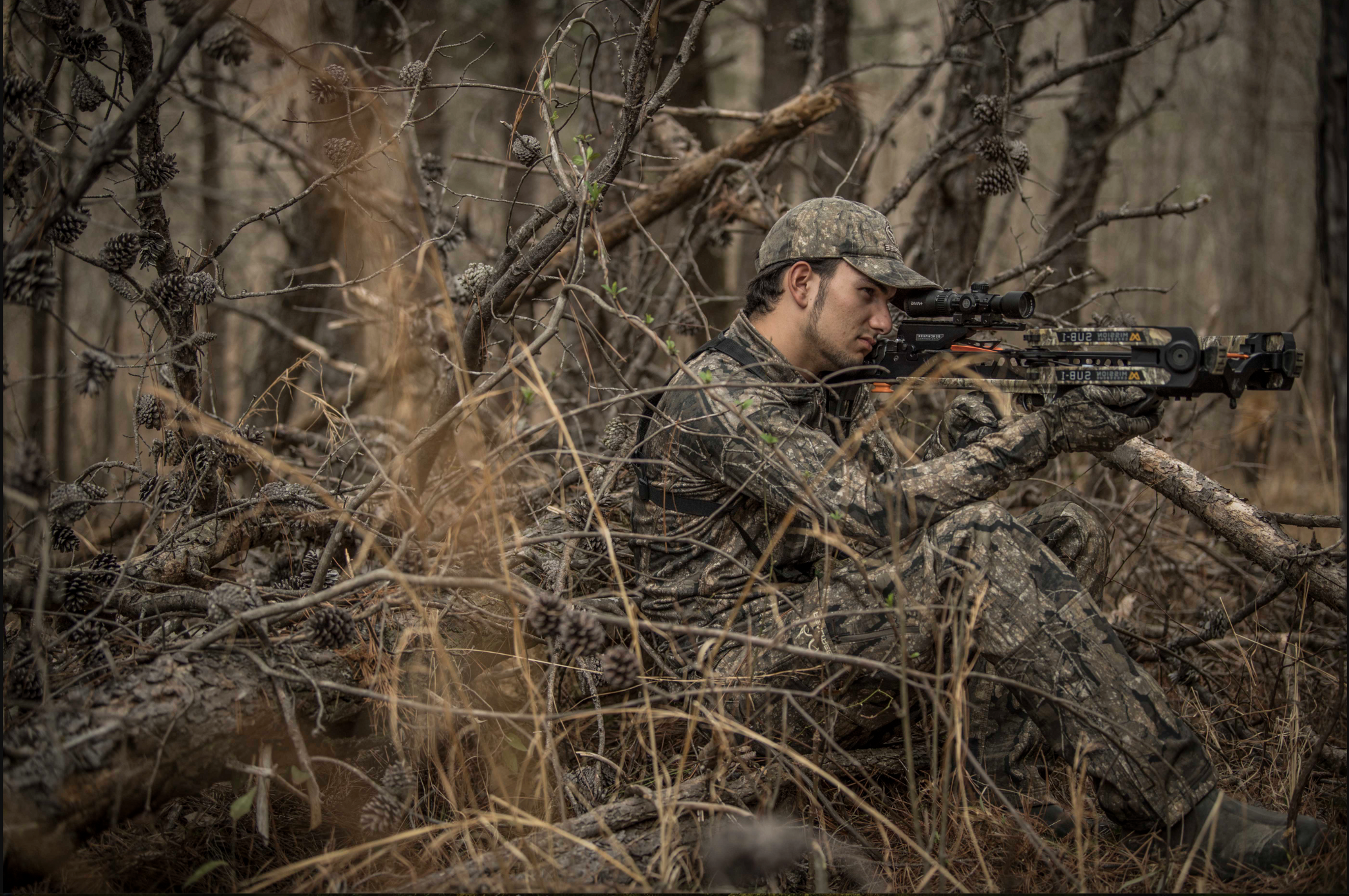 A hunter shoots a crossbow from a natural blind. 