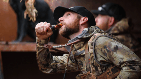 Hunter in camouflage gear blowing a duck call during a hunting session.