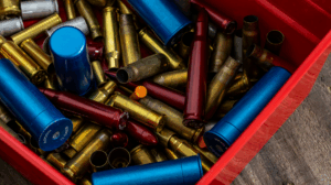 Red bin filled with mixed brass bullet casings and colorful snap caps