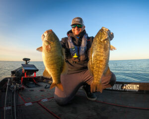 Angler holding two large smallmouth bass on fishing boat at sunrise