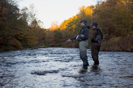 Two anglers fly fishing in a scenic autumn river wearing waders