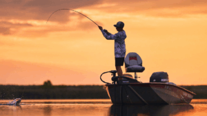 Angler casting fishing rod from Bass Tracker boat at golden sunset on calm lake