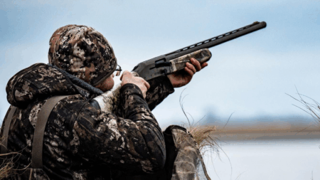 Best Black Friday Shotgun Deals of 2025 Hunter in camouflage gear aiming shotgun skyward during waterfowl hunting season outdoors.
