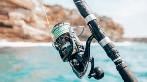 Close-up of spinning fishing reel with green line near ocean rocks