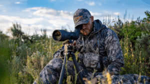 Hunter in camouflage using a spotting scope on tripod in wilderness field