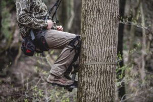 Hunter in camouflage sitting on a tree stand attached to forest tree.