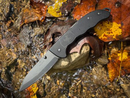 Victorinox black folding pocket knife displayed on autumn leaves near water