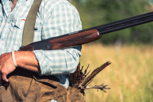 Hunter holding an over-under shotgun with harvested pheasant in field
