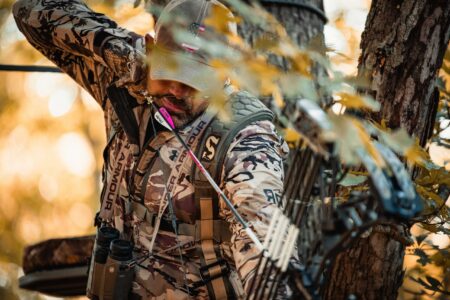 Hunter in Under Armour camo gear preparing arrows in a tree stand.
