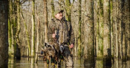 Chêne Waders Review: Are the $1,100 Waders Worth It? Hunter in camouflage wading through flooded forest carrying harvested mallard ducks.