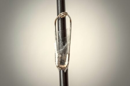 Clear quartz crystal pendant wire-wrapped onto a dark metal rod