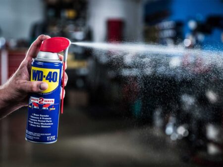 Hand spraying WD-40 multi-use lubricant product in a garage workshop setting