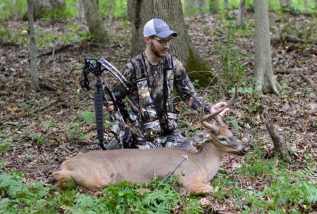 Hunter in camouflage posing with harvested white-tailed buck deer in forest