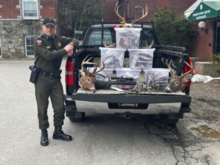 Game warden stands beside truck bed displaying confiscated deer heads and illegal hunting equipment.