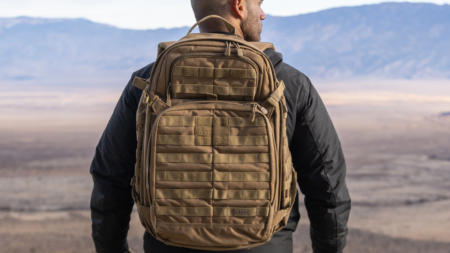 Man wearing tan tactical MOLLE backpack overlooking desert mountain landscape outdoors