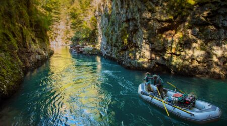 Two people fishing from an inflatable raft in a stunning rocky river canyon.