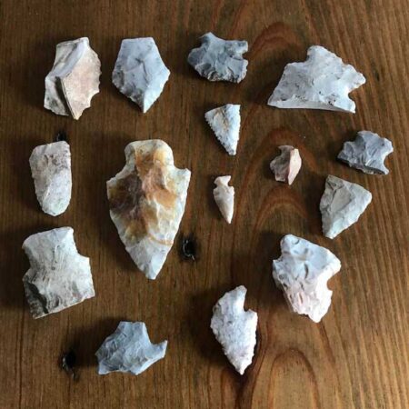 Find a 12,000-Year-Old Arrowhead With These 10 Tips Collection of ancient flint arrowheads and stone tools displayed on wooden surface