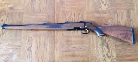 Bolt-action hunting rifle with walnut wood stock lying on hardwood floor