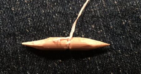 Small copper-colored pointed object with string attached lying on dark fabric surface