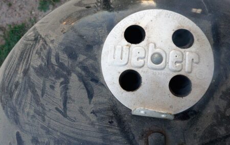 Weber charcoal grill lid with vents and branded logo plate close-up