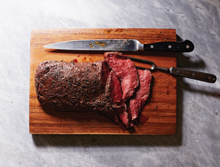Sliced rare roast beef on wooden cutting board with carving knife and fork