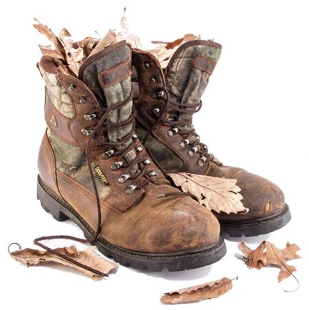 Worn Gore-Tex camouflage hunting boots surrounded by scattered dry autumn oak leaves