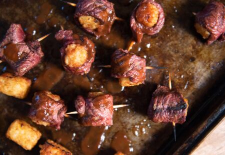 Seven Creative (and Easy) Wild-Game Popper Recipes Beef-wrapped tater tot bites on toothpicks glazed with BBQ sauce on baking sheet
