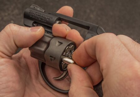Hands unloading bullets from an open revolver cylinder during maintenance