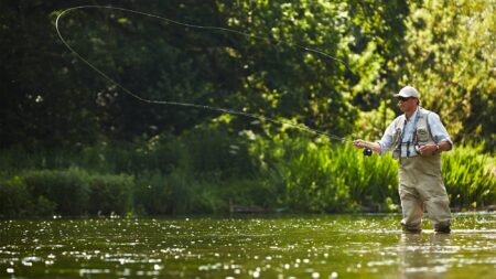 Man fly fishing in river with casting line arcing through air