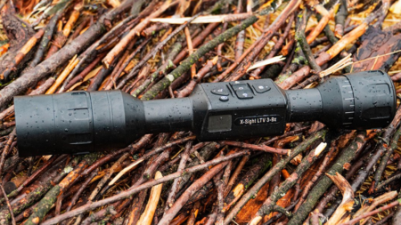 ATN X-Sight LTV 3-9x night vision rifle scope lying on wet branches outdoors