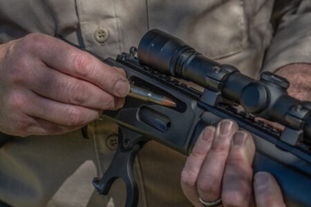 A .30/30 Is All You Need (If You Know How to Hunt) Person loading a bullet into a lever-action rifle with mounted scope.