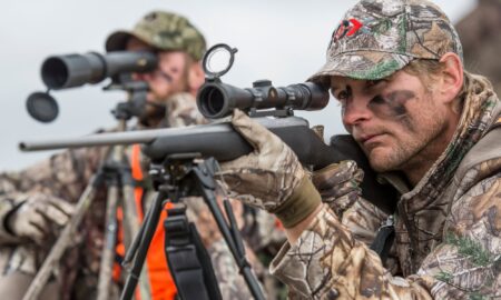 Two hunters in camouflage aiming rifles with scopes during a hunting expedition.