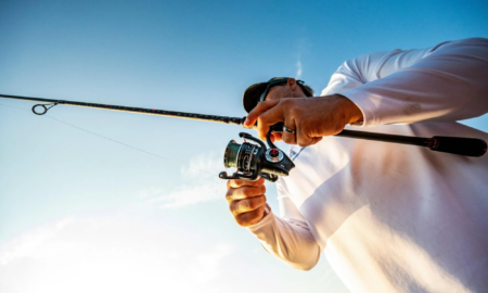 Man in white shirt fishing with spinning rod and reel against blue sky