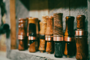 Handcrafted wooden duck calls with copper bands displayed on a rustic shelf.