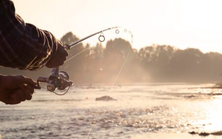 Person fishing at sunrise with spinning rod and reel near misty river