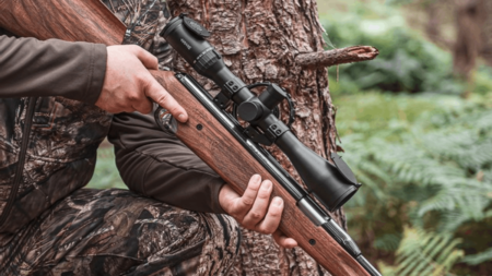 Hunter in camouflage holding bolt-action rifle with scope in forest setting