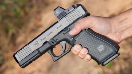 Hand holding a Glock 21 Gen 5 45 Auto pistol with red dot sight.