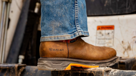 Person wearing brown Ariat work boot stepping on industrial equipment outdoors.