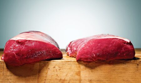 Two raw red beef cuts resting on a wooden cutting board