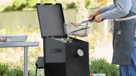 Person using tongs to lift food basket from outdoor deep fryer cooker
