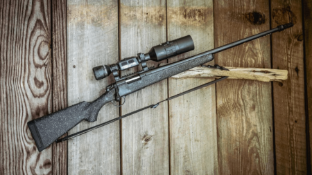 Bolt-action rifle with scope and sling resting on rustic wooden surface