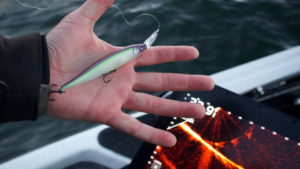 6 Forward-Facing Sonar Baits To Help You Catch More Fish Person holding a shiny green fishing lure with treble hooks over water
