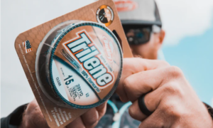 Man holding Berkley Trilene 15lb 100% fluorocarbon fishing line spool outdoors.